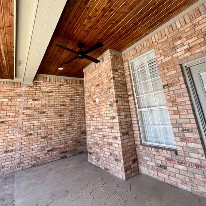 Covered brick porch with wood ceiling, ceiling fan, and window on a brick exterior wall.