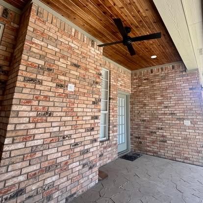 Brick porch with wood ceiling, black ceiling fan, and white door