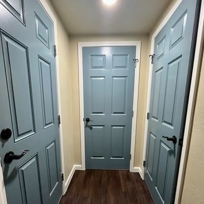 Narrow hallway with three light blue doors and dark wood flooring