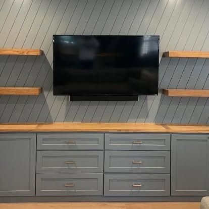 Wall-mounted TV above a gray cabinet with drawers and side doors against a wood-paneled wall.