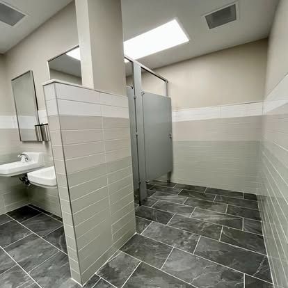 Modern public restroom with tiled stalls, sinks, and gray flooring