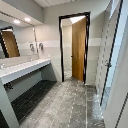 Modern restroom with gray tile floor, white sinks, mirrors, and a partially open wooden door
