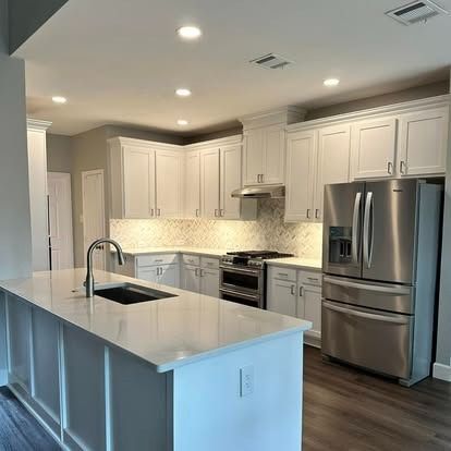 Modern white kitchen with island, stainless steel appliances, and dark wood flooring