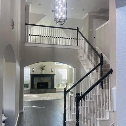 Bright foyer with curved staircase, white railings, chandelier, and view into a living room with fireplace.