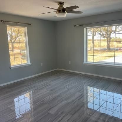 Empty gray room with glossy wood floor, ceiling fan, and two windows letting in daylight