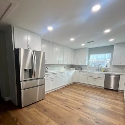 Bright modern kitchen with white cabinets, stainless steel appliances, and wood flooring