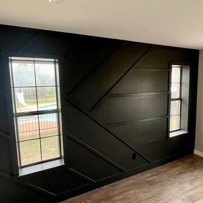 Black painted wall with geometric trim and two tall windows overlooking a yard