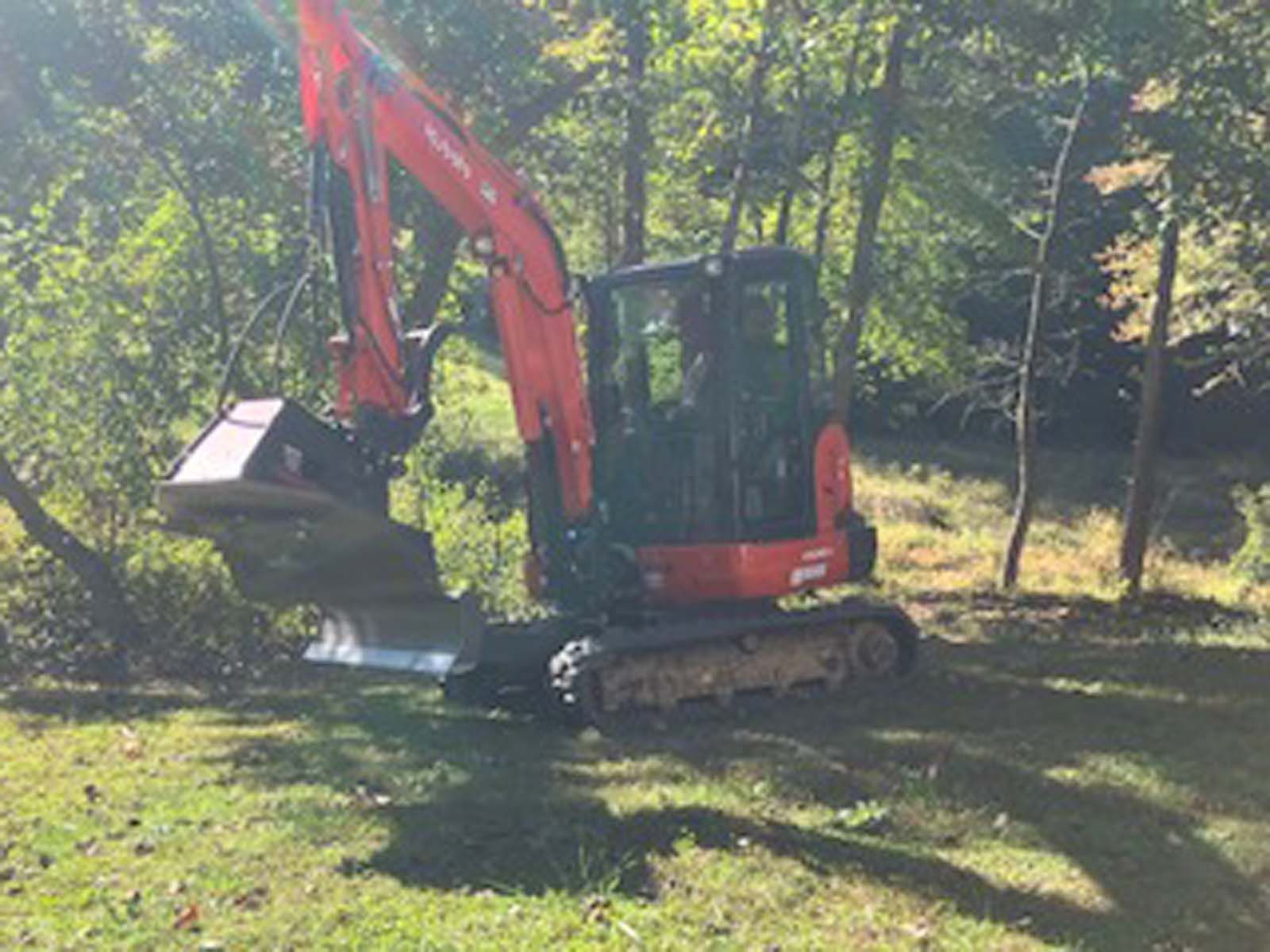 A red excavator is sitting on top of a lush green field.