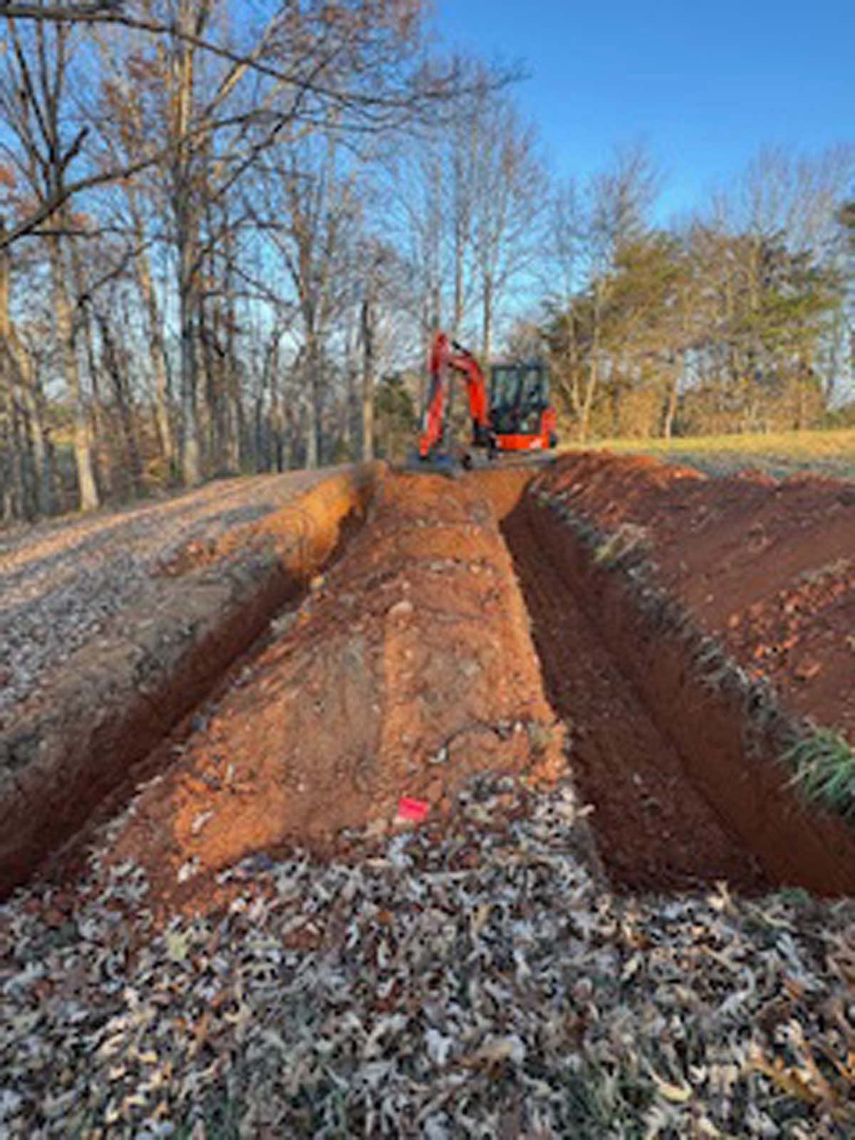 A red excavator is digging a trench in the dirt.