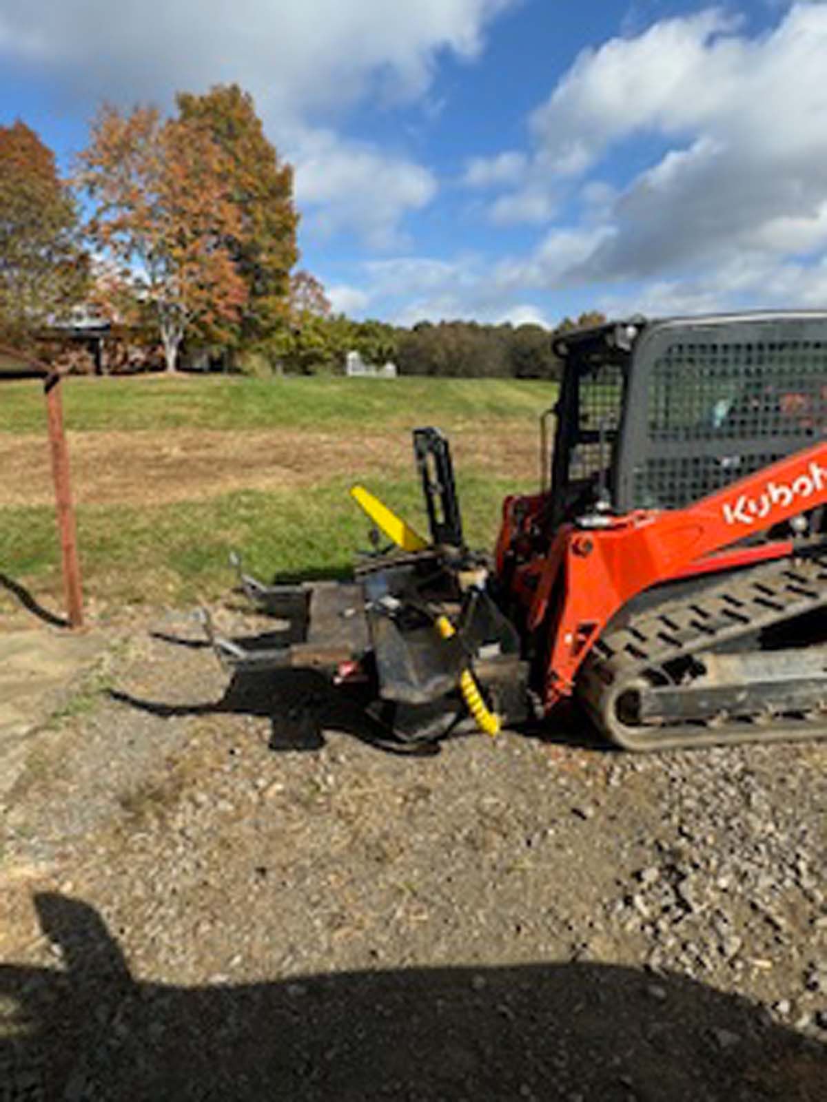 A red and black kubot skid steer is parked in a dirt field.