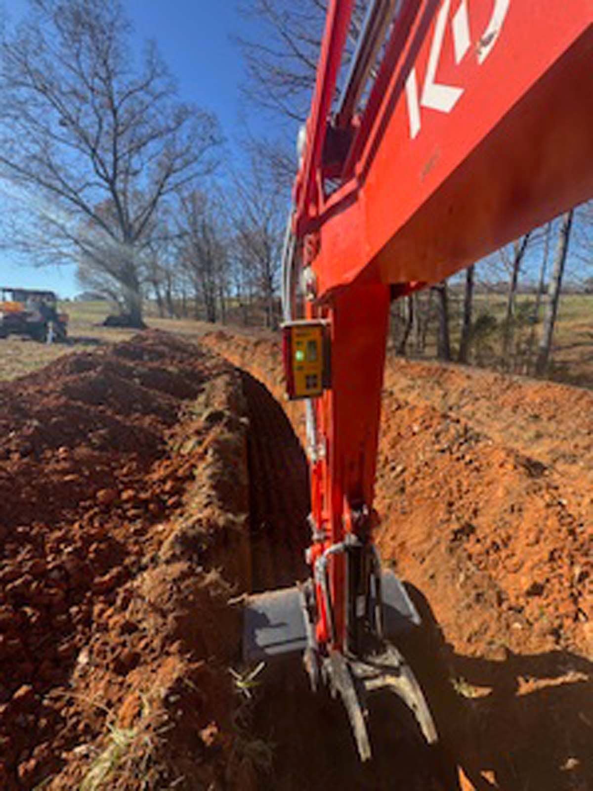 A red excavator is digging a hole in the dirt.