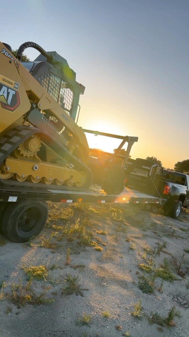 Yellow Caterpillar skid steer on a trailer with the sun setting in the background.