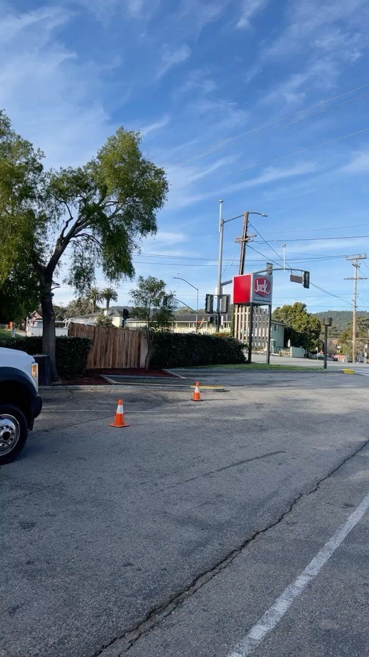 A view of a street corner with a red sign, greenery, and traffic cones on the road.
