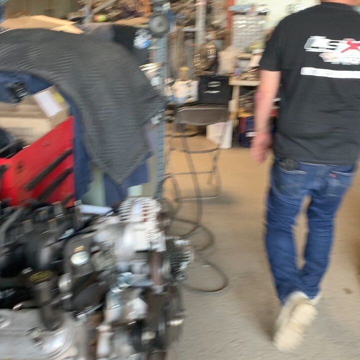 Engine assembly in a workshop with a person wearing a black LSX t-shirt and jeans walking past.