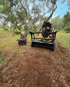 A small tractor with an attachment toothed blade, preparing a trail in a wooded area.