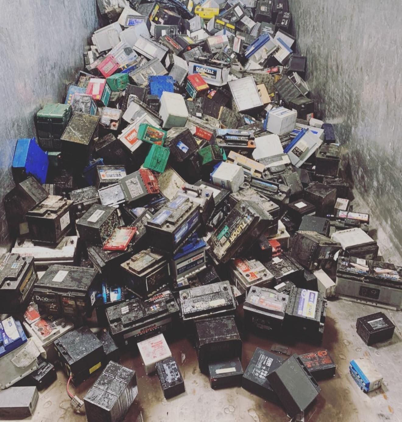 Un grande mucchio di batterie al piombo per auto usate di vario tipo, stoccate all'interno di un contenitore per il riciclaggio.