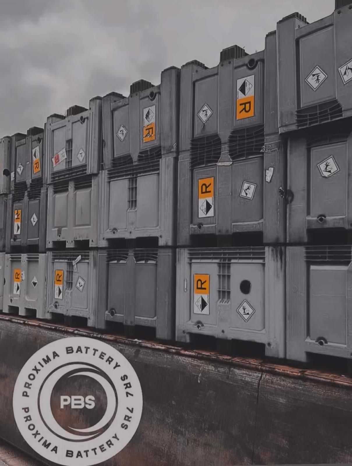 Una pila di contenitori industriali grigi con etichette gialle di pericolo chimico, contrassegnate dal logo Proxima Battery SRL.