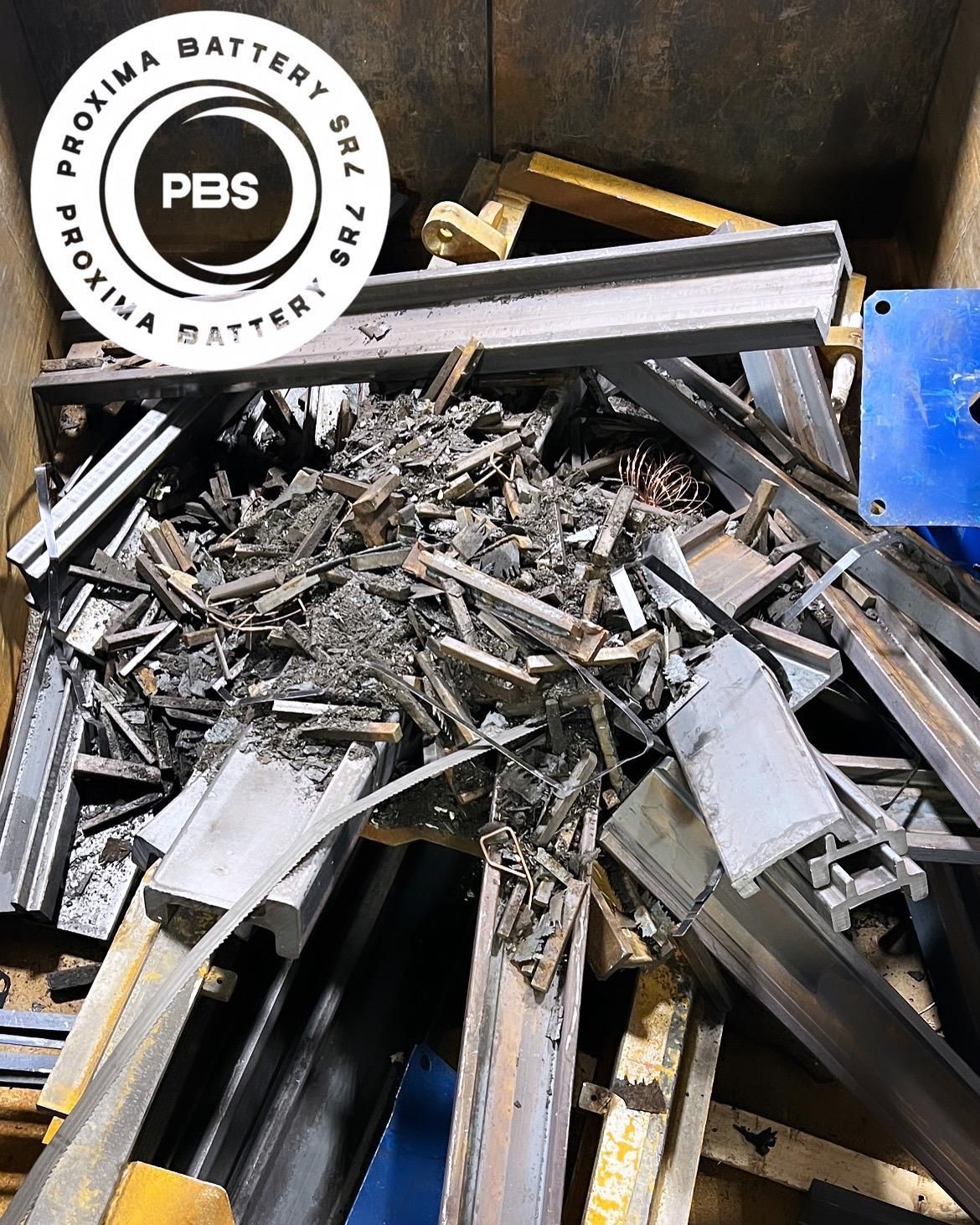 Un mucchio di rottami metallici, tra cui travi e trucioli di metallo, all'interno di un container con il logo Proxima Battery in un angolo.