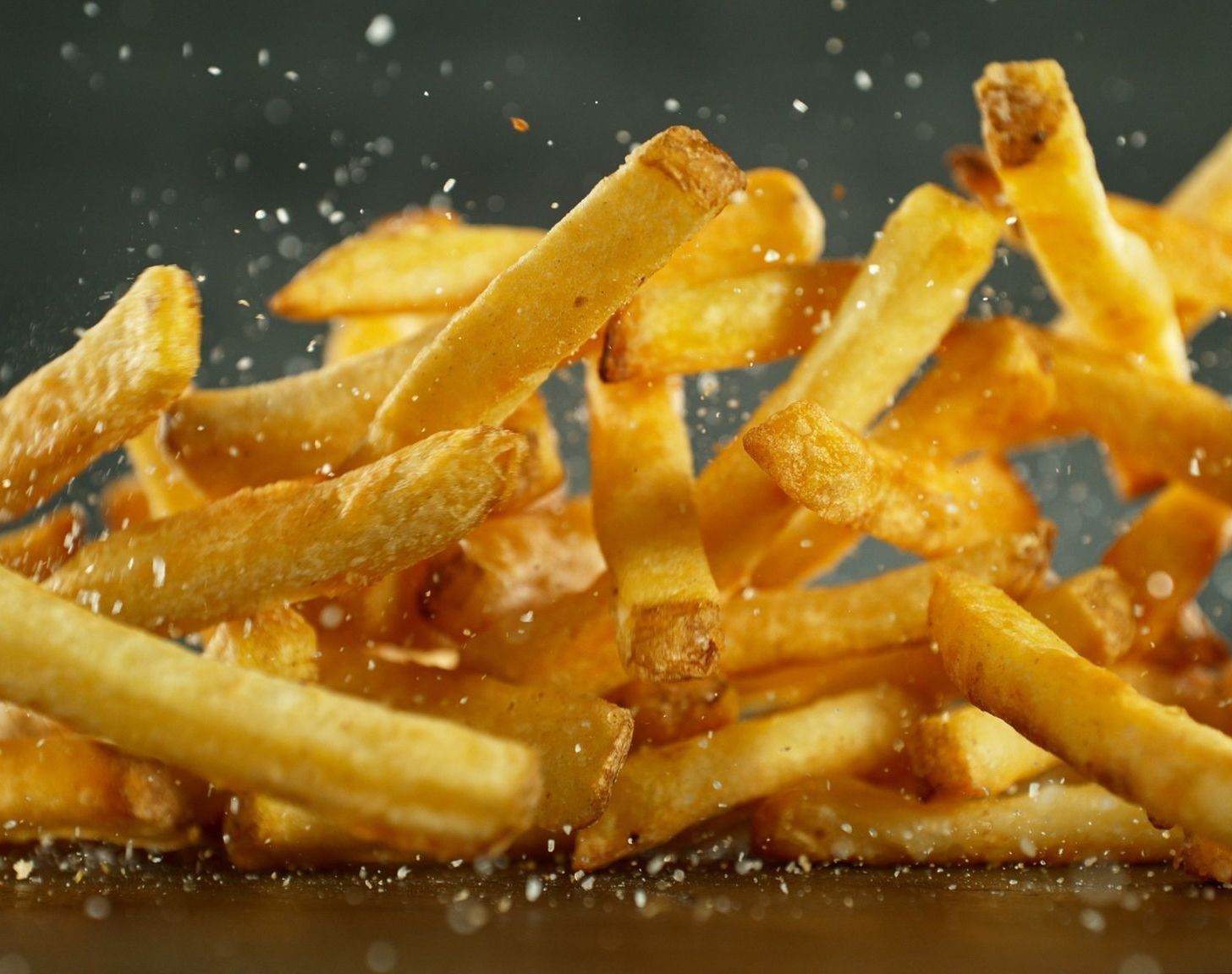 Goldene Pommes Frites in der Luft, verstreut, mit Salzpartikeln.