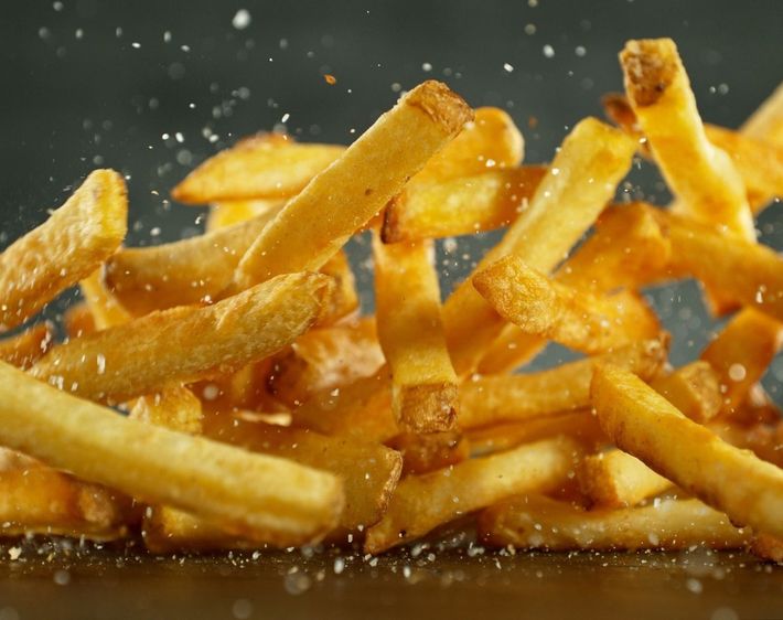 Goldene Pommes Frites in der Luft, verstreut, mit Salzpartikeln.