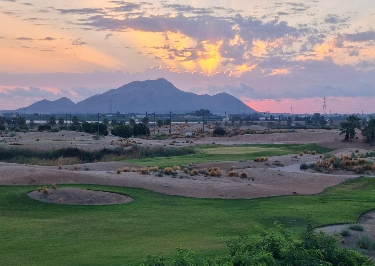 a view of a golf course at sunset with mountains in the background .