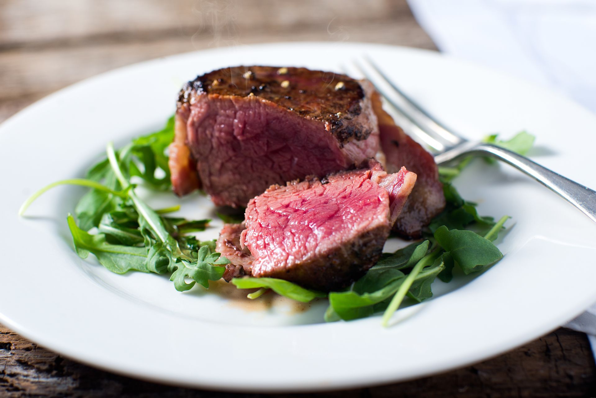 A white plate topped with steak and greens with a fork.