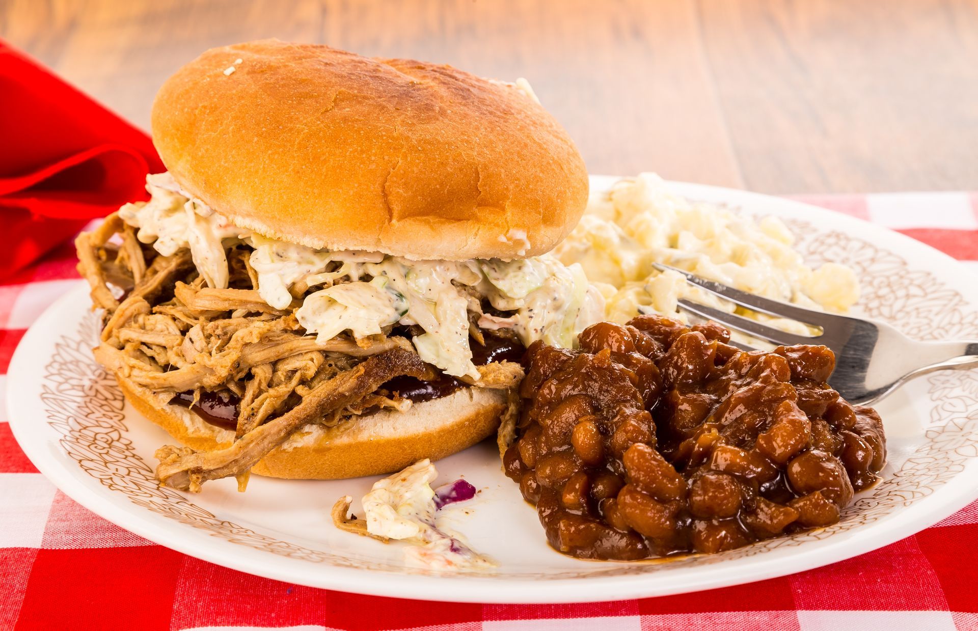 A pulled pork sandwich with coleslaw and baked beans on a plate.