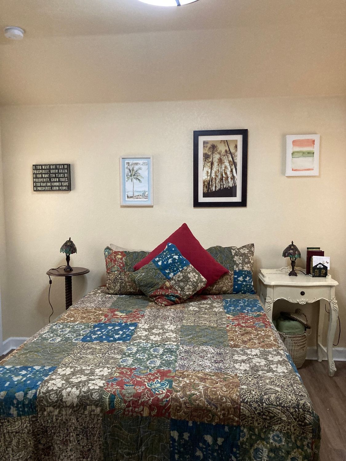 A bedroom with a bed , nightstand , lamps and pictures on the wall.