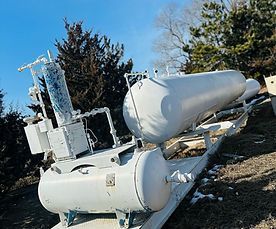 A bunch of white tanks are sitting on top of each other in a field.