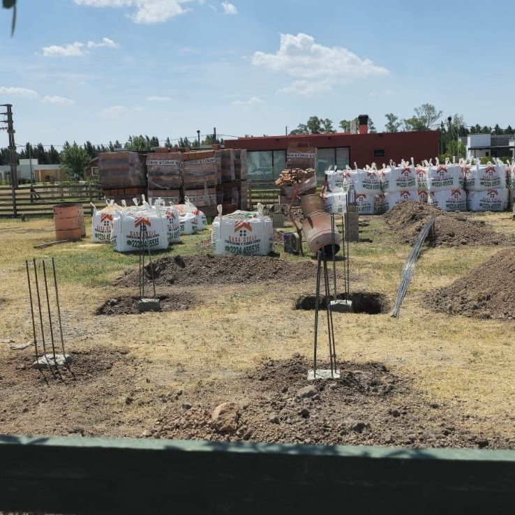 Obra en construcción con zapatas de hormigón, barras de refuerzo y materiales como ladrillos y sacos.