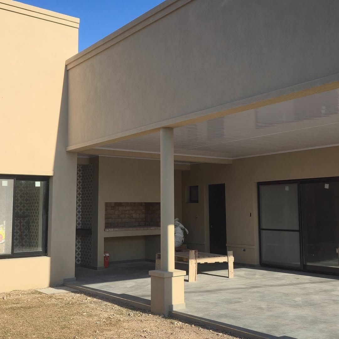 Exterior de casa color beige con patio abierto, parrilla y puertas corredizas de vidrio.