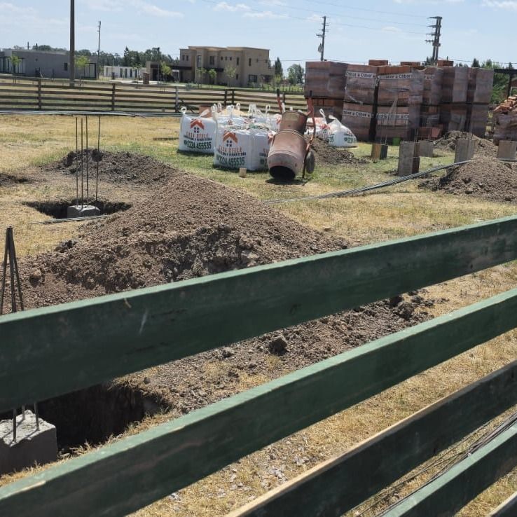 Obra en construcción con cimientos de hormigón, barras de refuerzo, sacos de materiales y ladrillos