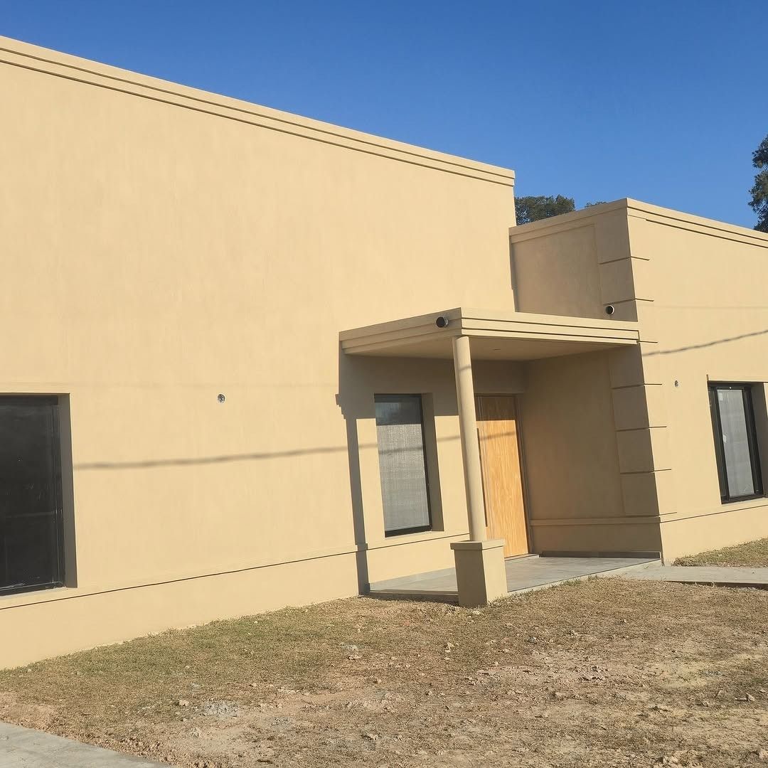 Edificio comercial color beige con entrada cubierta, ventanas y zona ajardinada.