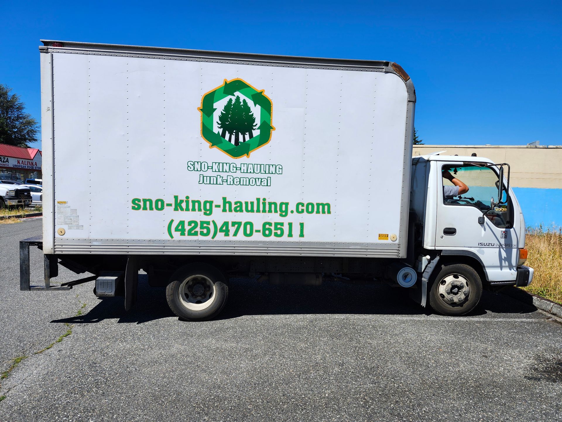 A white hauling truck parked on pavement, featuring a green logo, 