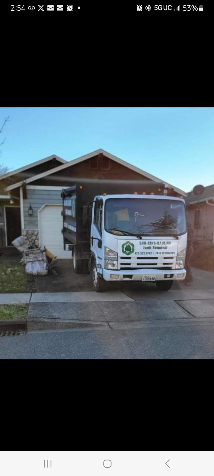 A white commercial dump truck parked in the driveway of a residential house under a clear blue sky.