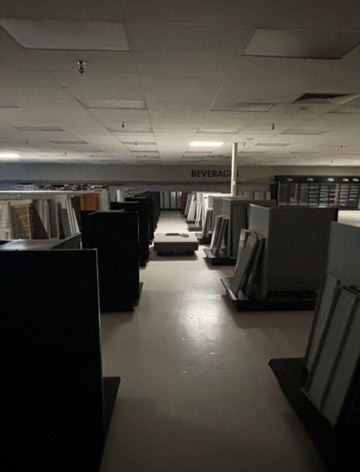 Dimly lit warehouse aisle with rows of standing display panels under a drop ceiling with scattered light panels.
