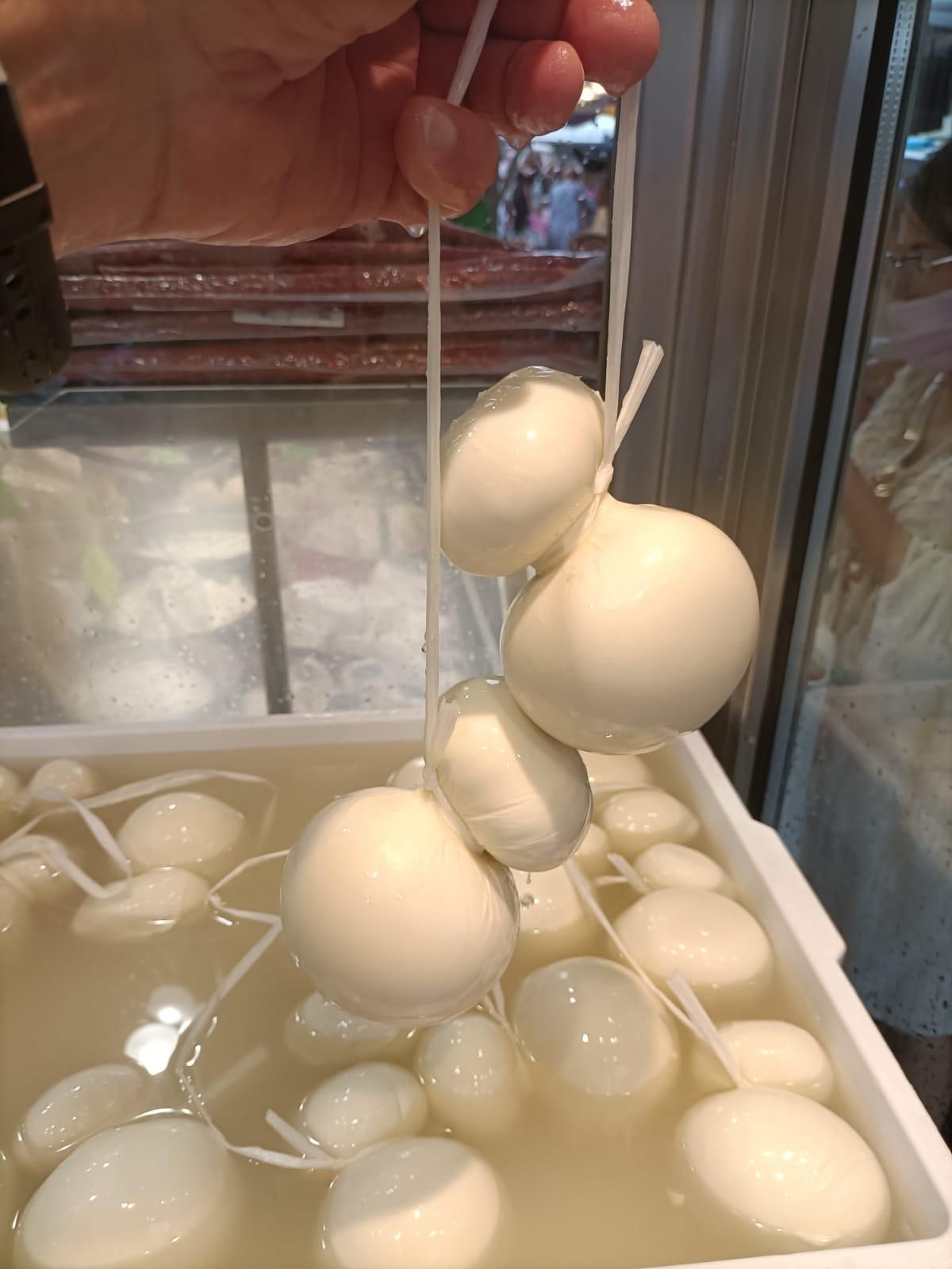 Una persona tiene una striscia di formaggio sopra un contenitore di palline di formaggio.