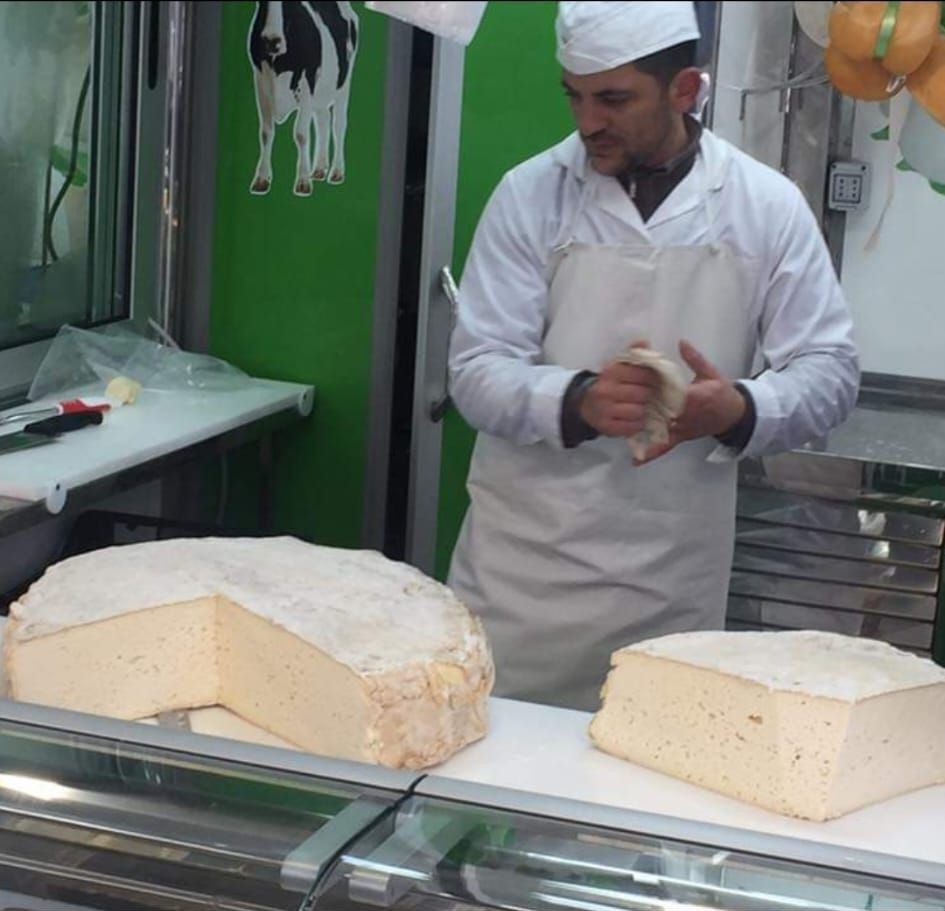 Un uomo con un grembiule bianco è in piedi davanti a un'esposizione di formaggi