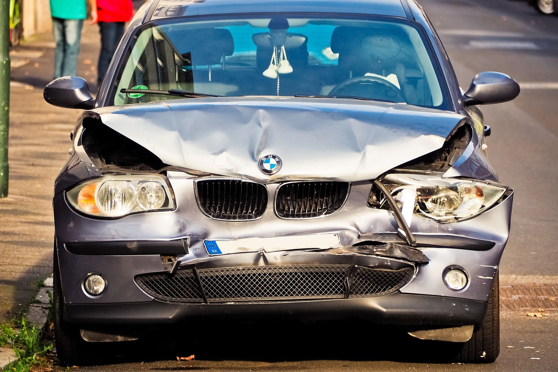 A bmw with a damaged front end is parked on the side of the road.