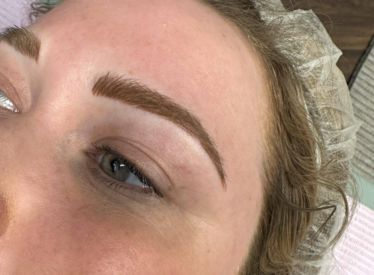 Close-up of a person's eye and eyebrow after eyebrow microblading; the eyebrow is brown.