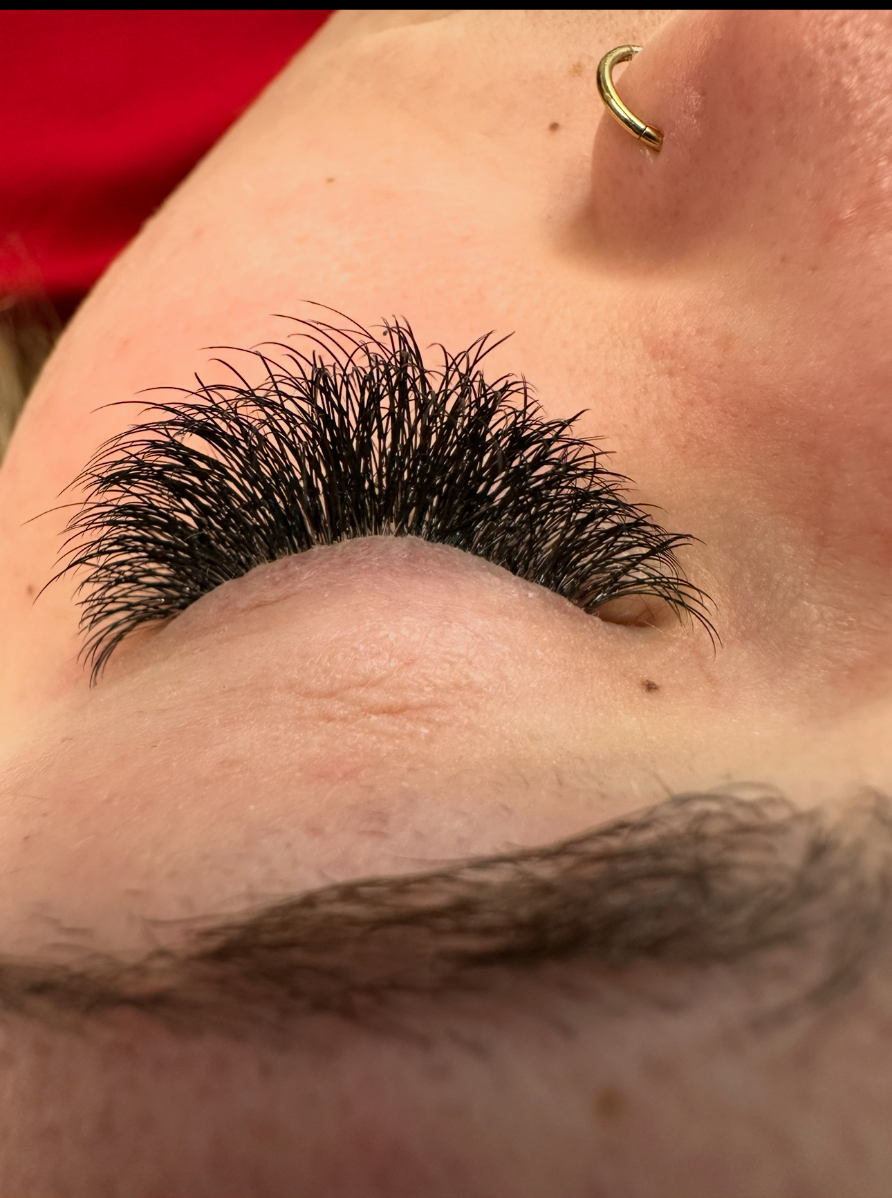 Close-up of eye with thick, dark eyelash extensions and a gold nose ring.