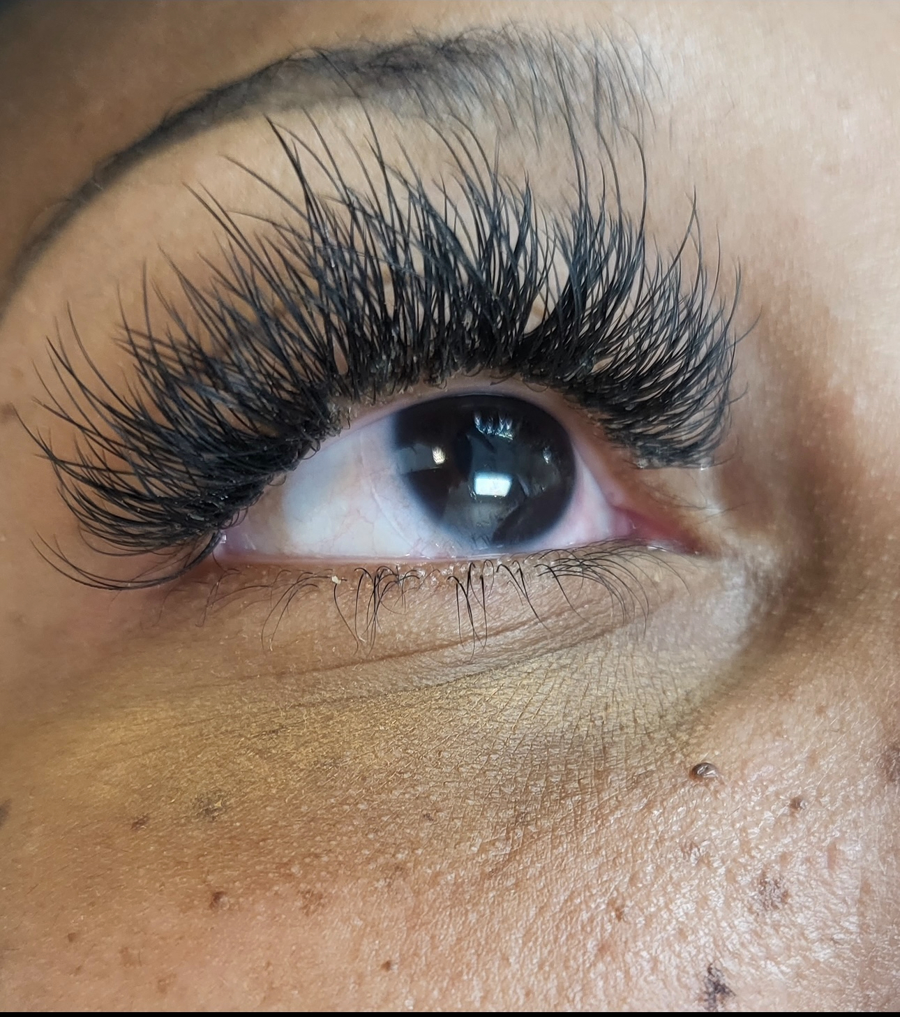 Close-up of an eye with thick, dark eyelash extensions; skin is tan.