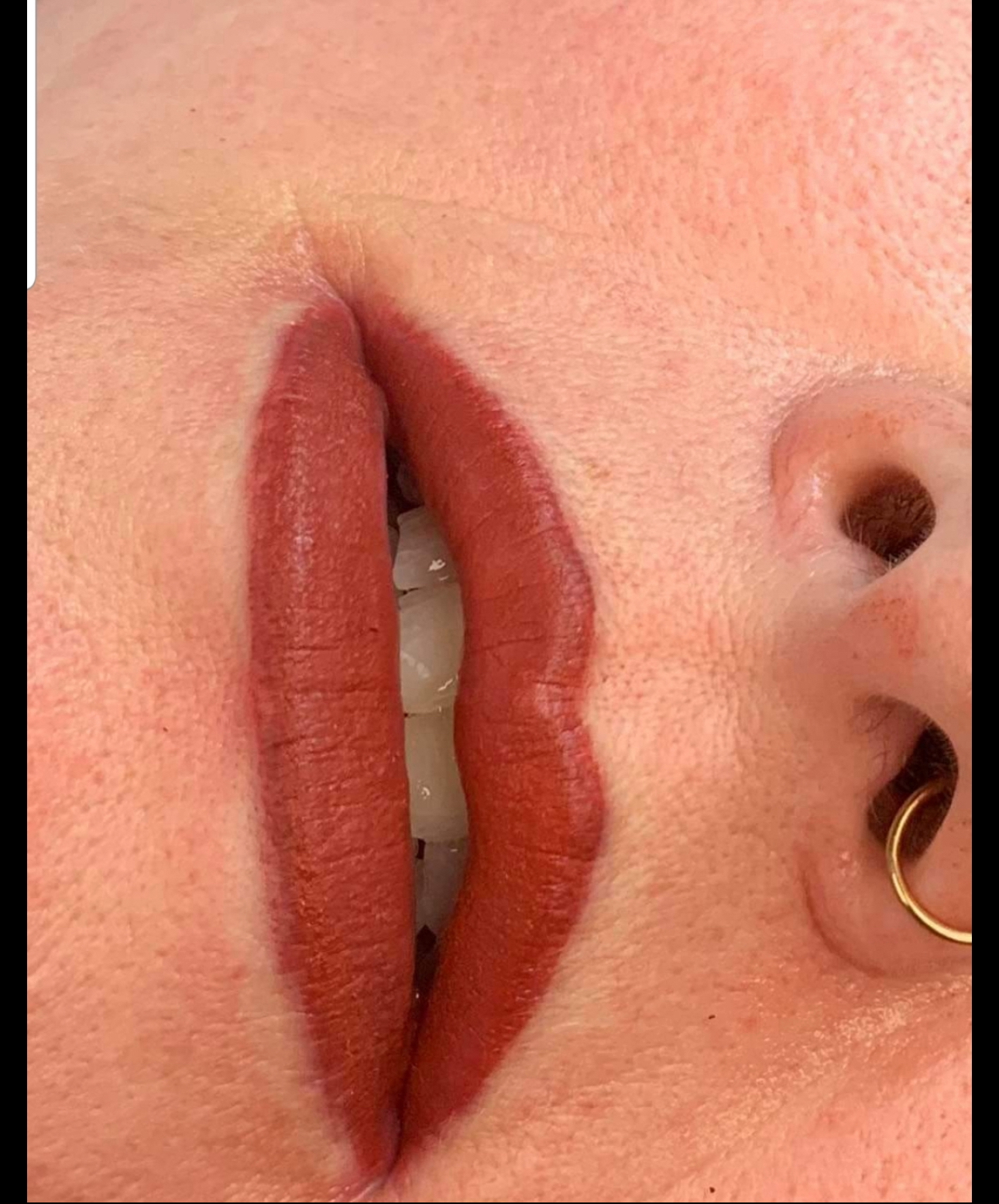 Close-up of a person's lips with red lipstick, visible teeth, and ear with a gold hoop earring.