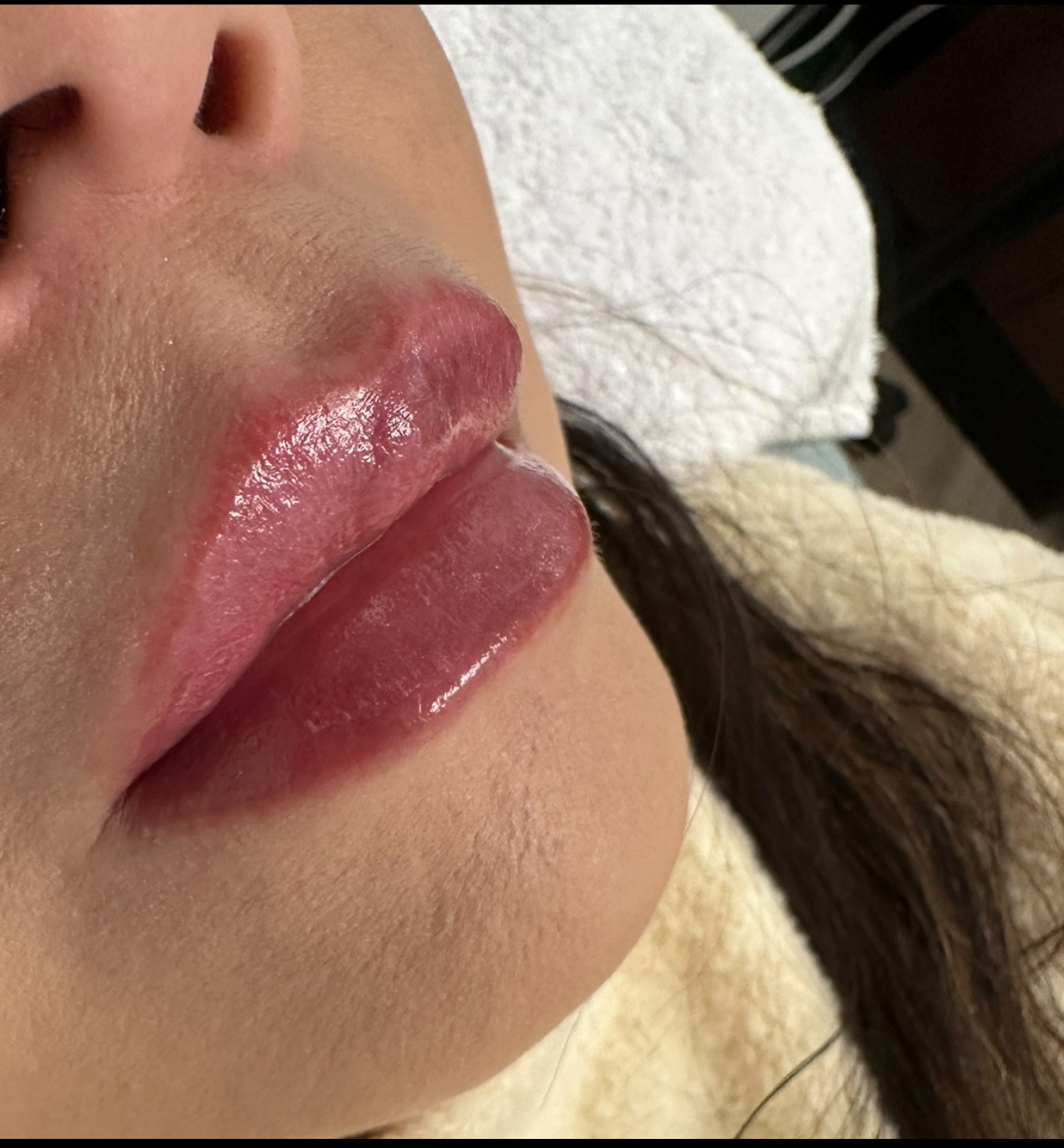 Close-up of a person's lips, glistening with pink pigment. They are slightly parted against a white towel.