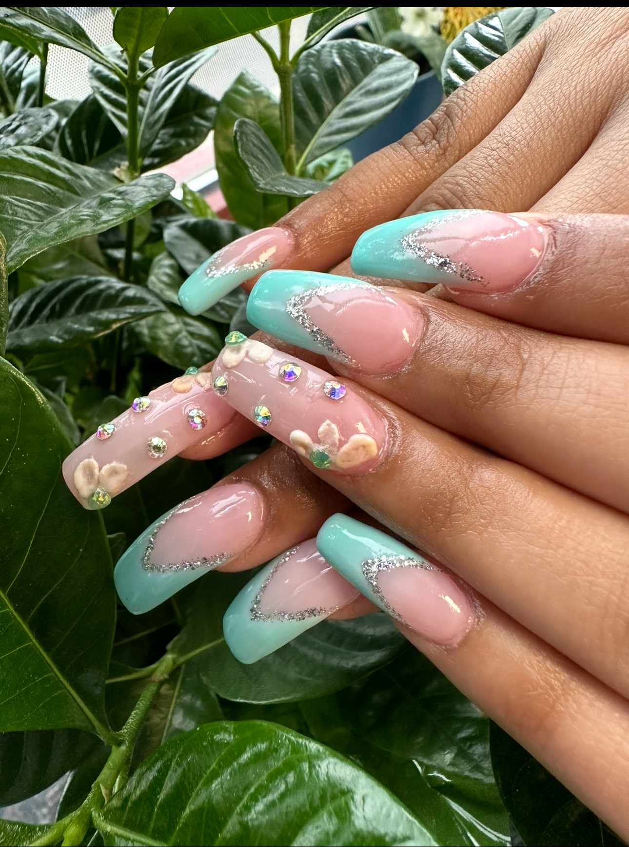 Close-up of manicured nails in a light blue and pink design, some with glitter and floral accents.