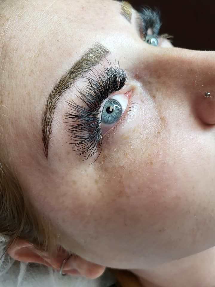 Close-up of a person's eye with thick, dark eyelashes, eyebrow, and blue iris.