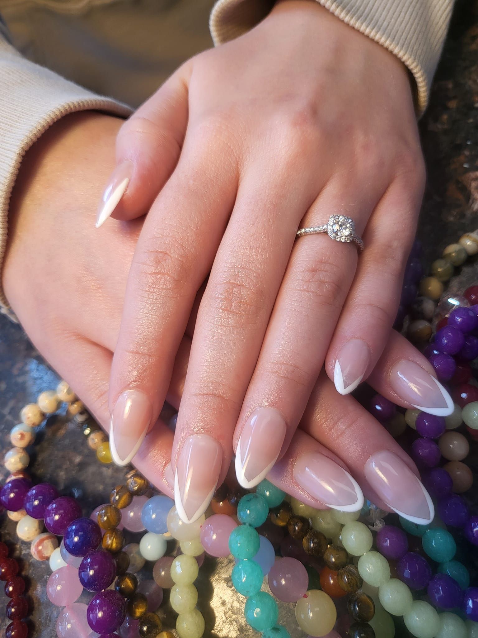 Hands with French tip nails, diamond ring, resting on a bed of colorful beads.