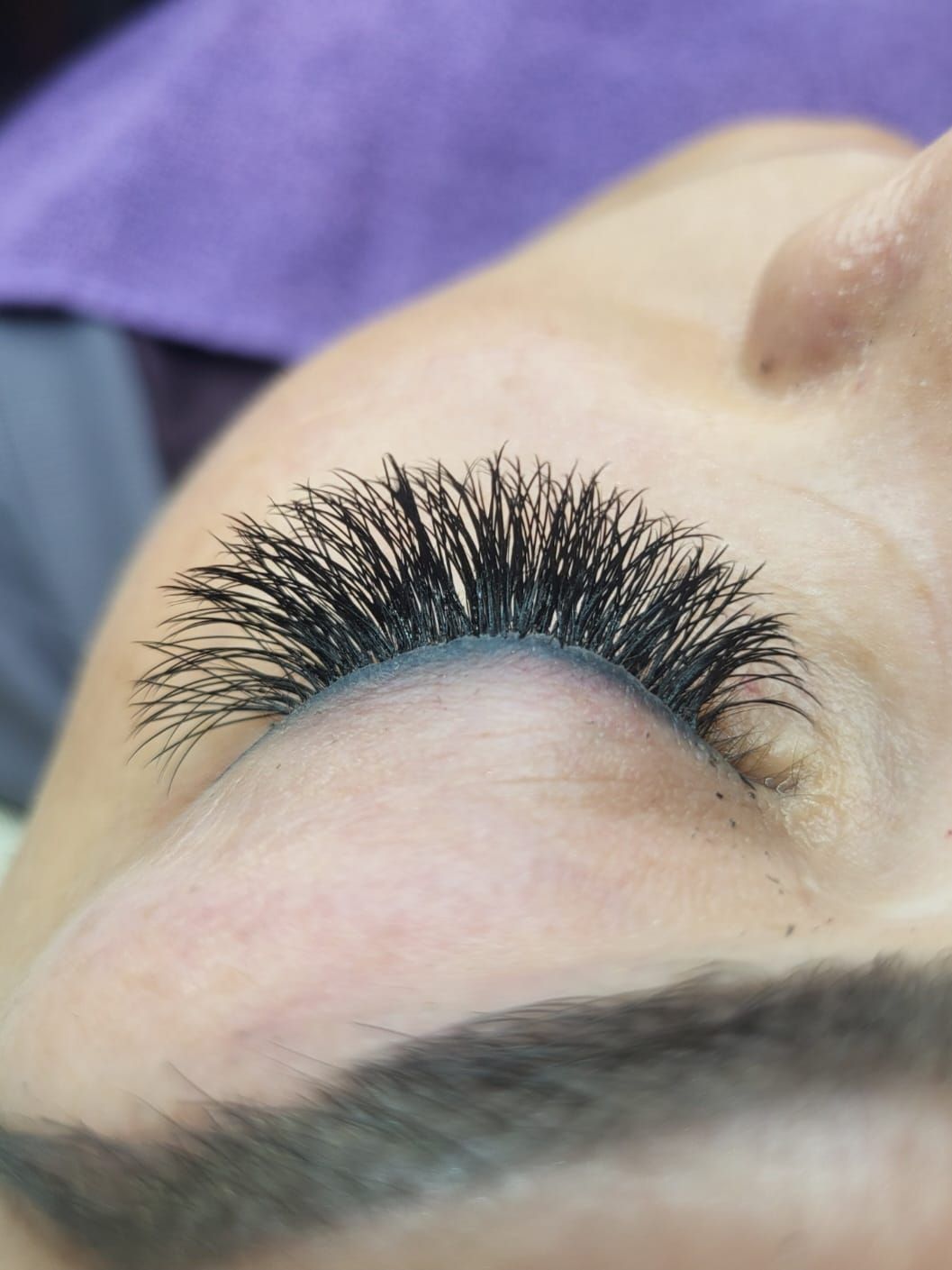 Close-up of closed eye with thick, black eyelash extensions. Purple surface in background.