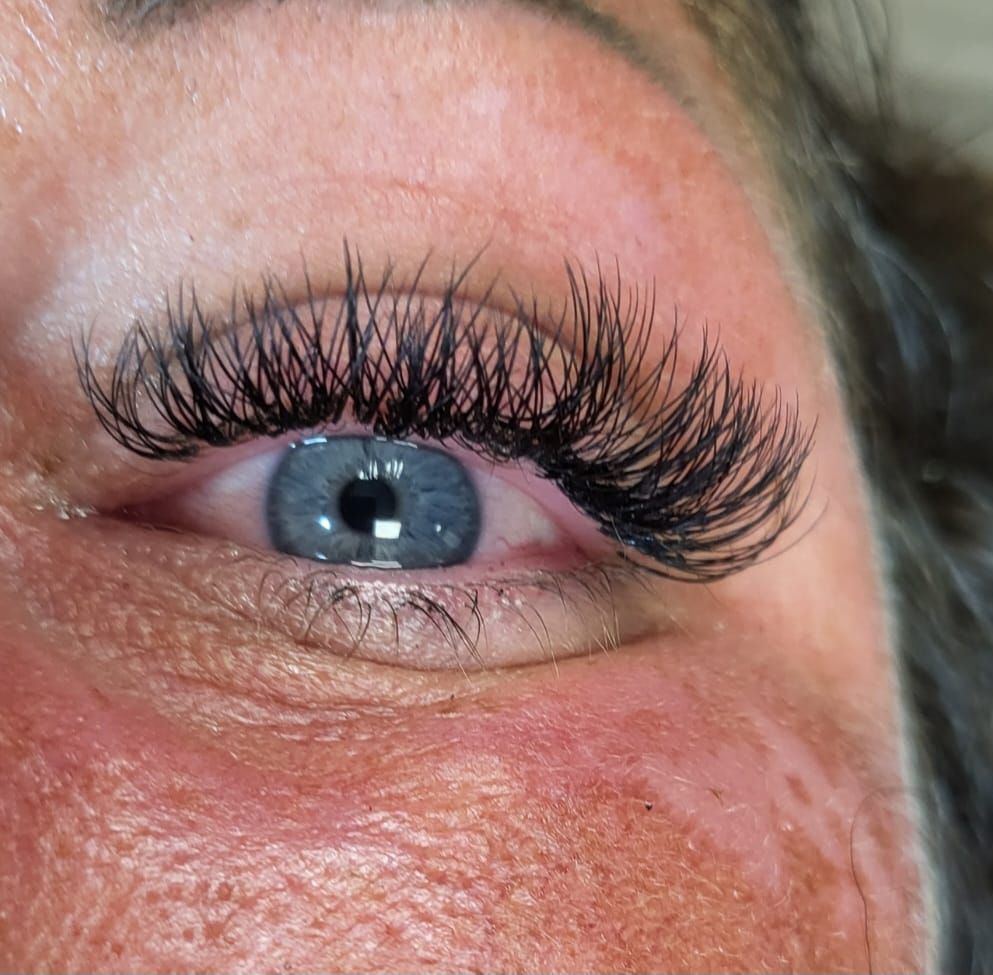 Close-up of a blue eye with long, black eyelash extensions, against a light skin tone.