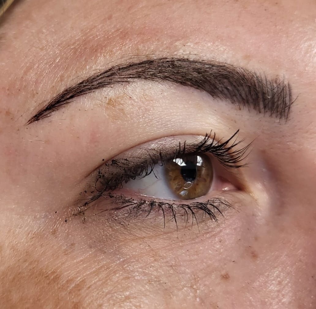 Close-up of an eye and eyebrow with cosmetic tattooing. The eyebrow is dark, and the eye has visible eyelashes.